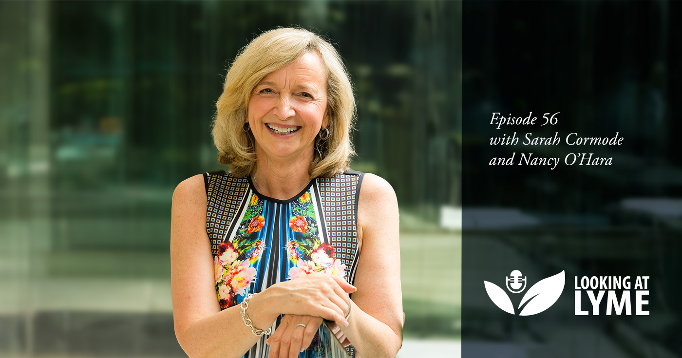 Dr. Nancy O'Hara stands in an open office area with her hands folded over a pane of glass and the beautiful greenery from the park behind her shines through.